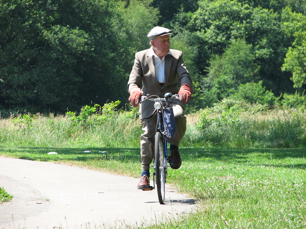 older man pedaling on a blue bicycle wearing a suit and beret