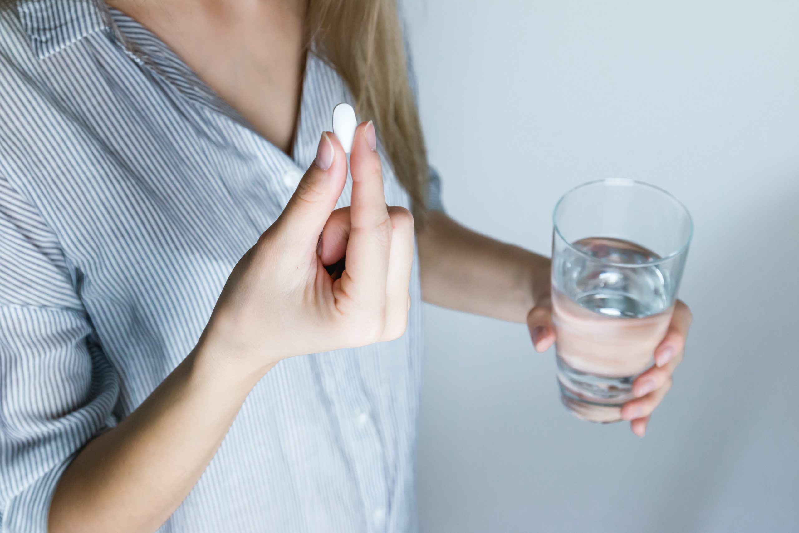 A woman holds a white pill and a glass of water.