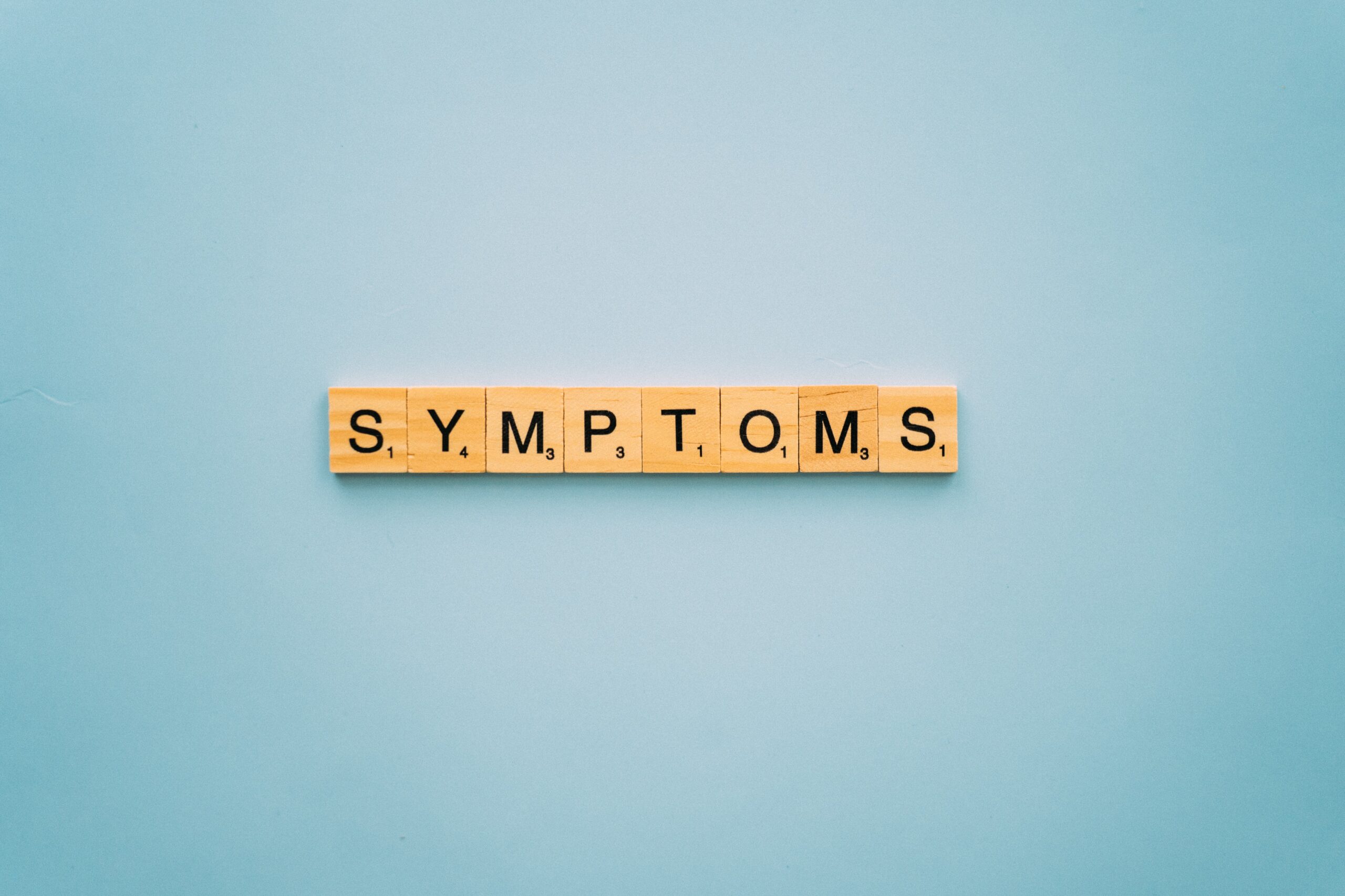 the word 'symptoms' spelled out in scrabble tiles.